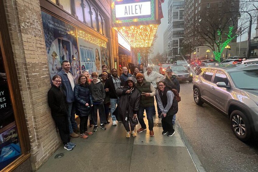 A group of people standing in front of a theater with a marquee that reads 'AILLEY'. 2