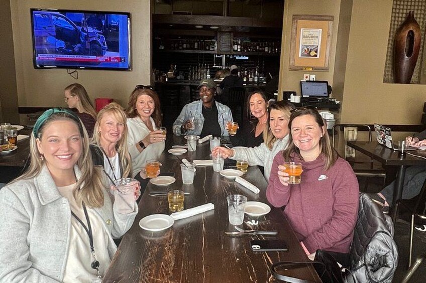 A group of people seated at a bar with drinks, a television mounted on the wall, and a bar counter with bottles. 3