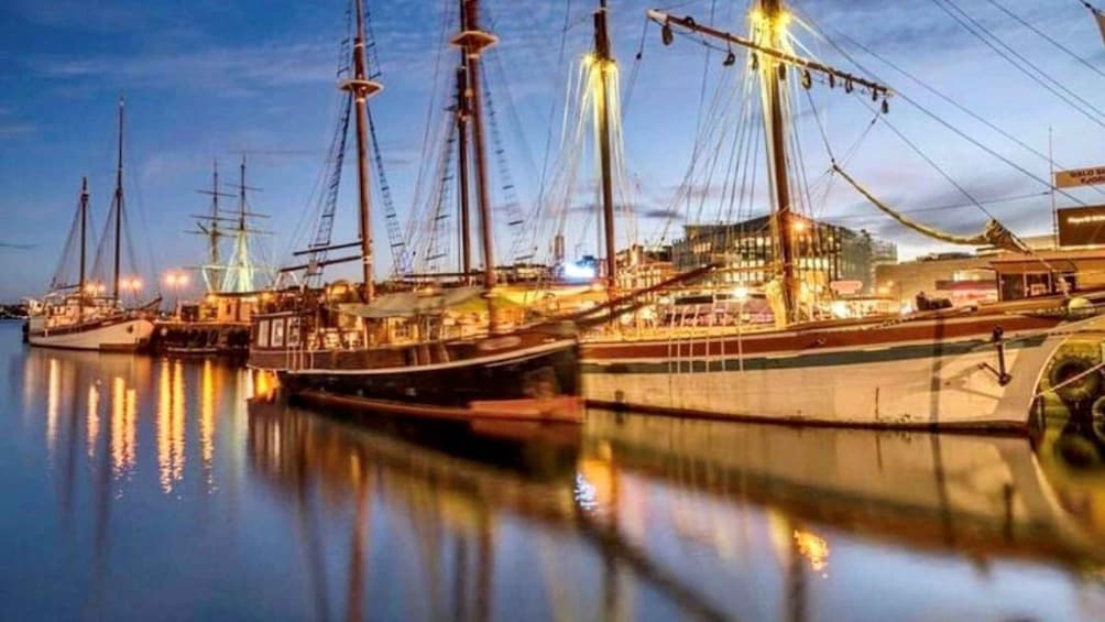 A marina at dusk with several tall ships docked, reflecting in calm waters. 5