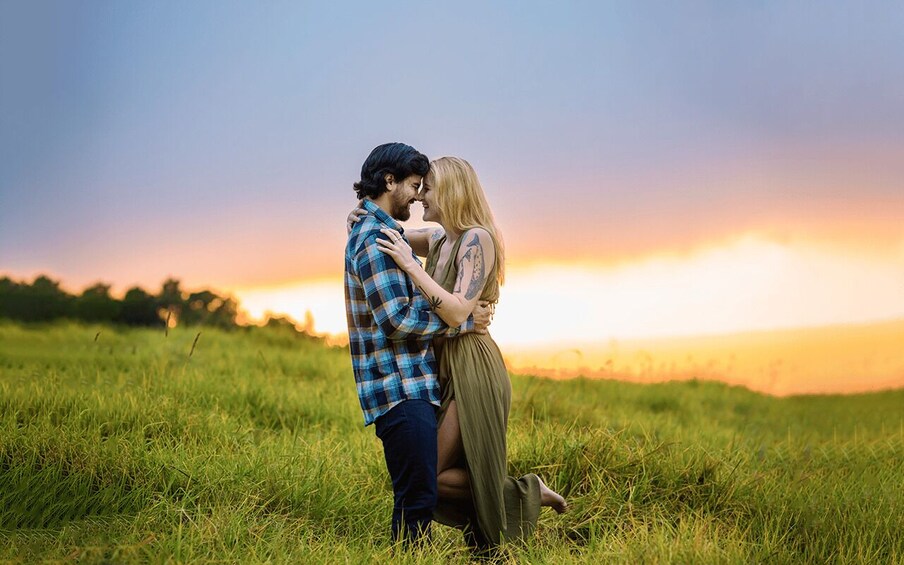 A couple embracing in a grassy field with a sunset in the background. 5