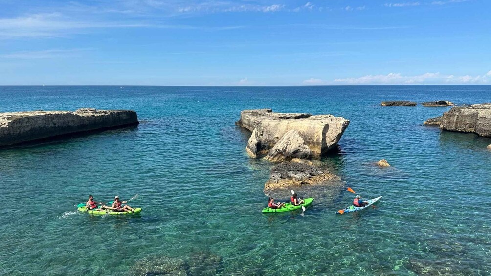 Kayakers on a calm sea with clear water, surrounded by rocky formations. 1