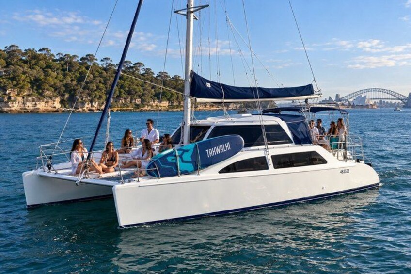 A white catamaran named TRHWAHLHI sailing on calm waters with a group of people on board. 3