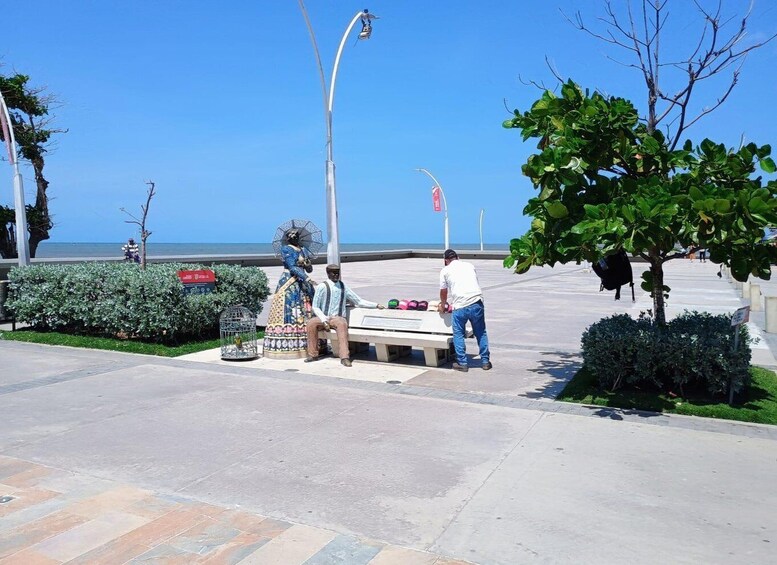 A statue of a man and woman on a bench, a street lamp, and a tree. 4