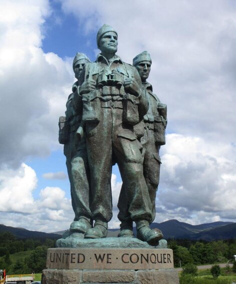 A bronze statue of three soldiers with a plaque reading 'UNITED WE CONQUER' in a mountainous landscape. 2