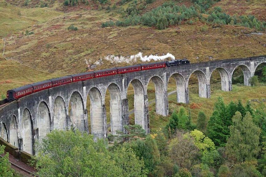 A train crossing a stone viaduct over a hilly landscape. 3