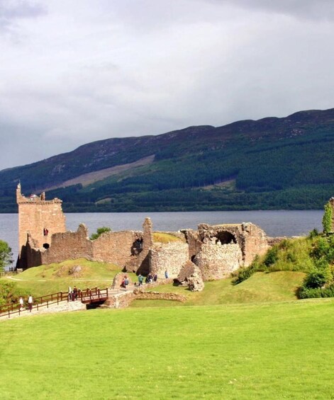 A historic castle ruin by a lake with a grassy foreground and hills in the background. 5