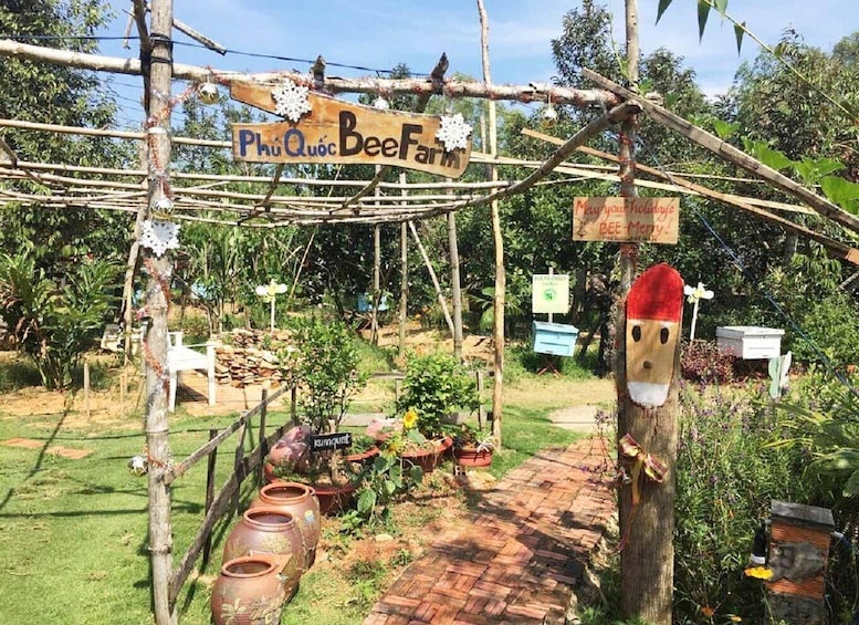 A rustic beekeeping setup with a wooden sign reading 'Phu Quoc Bee Farm,' beehives, and a bee costume decoration. 3