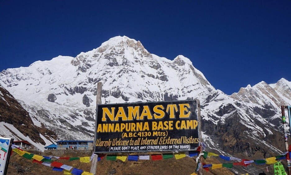 En skylt med texten ”Namaste Annapurna Base Camp” och en bakgrund av snötäckta berg. 5