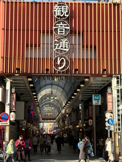 A covered pedestrian walkway with people walking, signs in Japanese, and a red structure overhead. 2