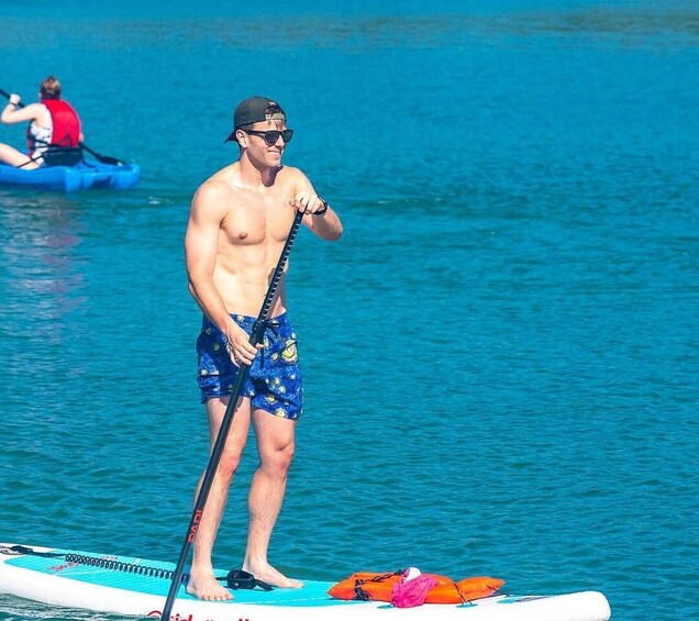 A man standing on a paddleboard in a body of water, holding a paddle. 5
