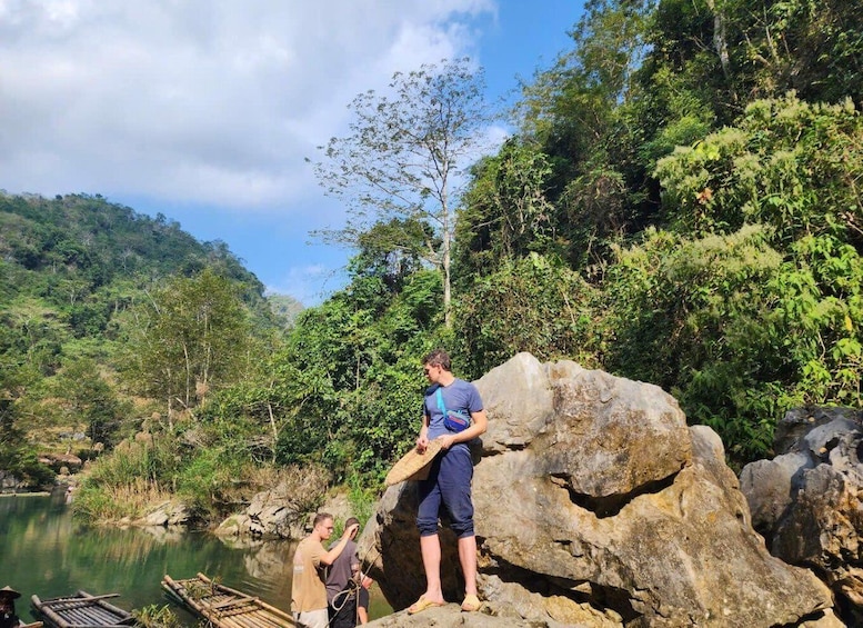 Two people standing on a large rock by a calm river surrounded by lush greenery. 4