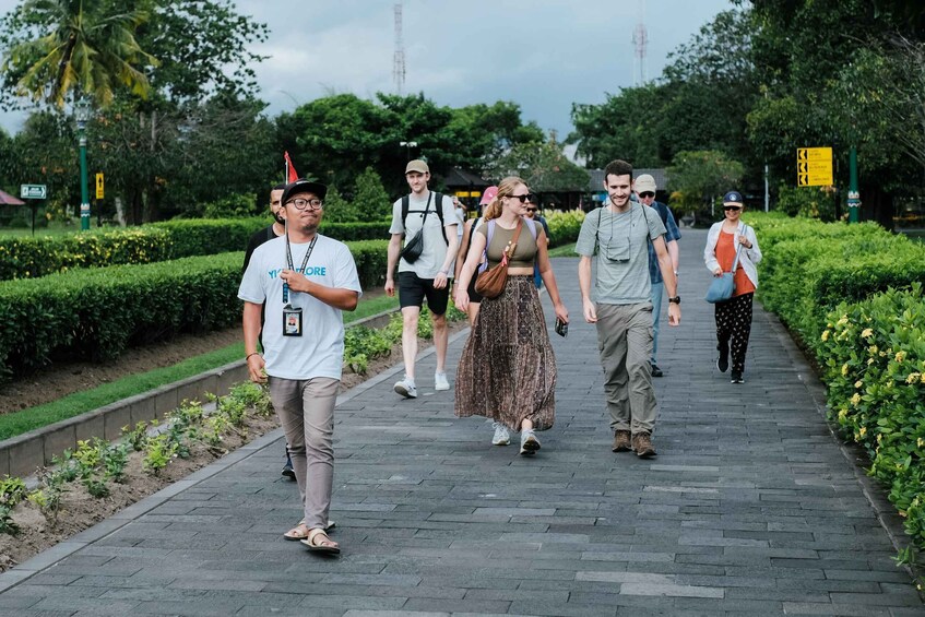 A group of people walking on a paved pathway in a park with greenery and trees. 1
