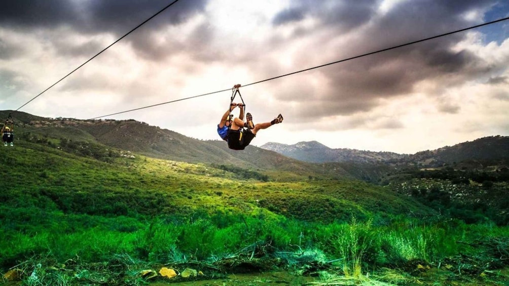 A person suspended in mid-air by a cable, with a mountainous landscape in the background. 1