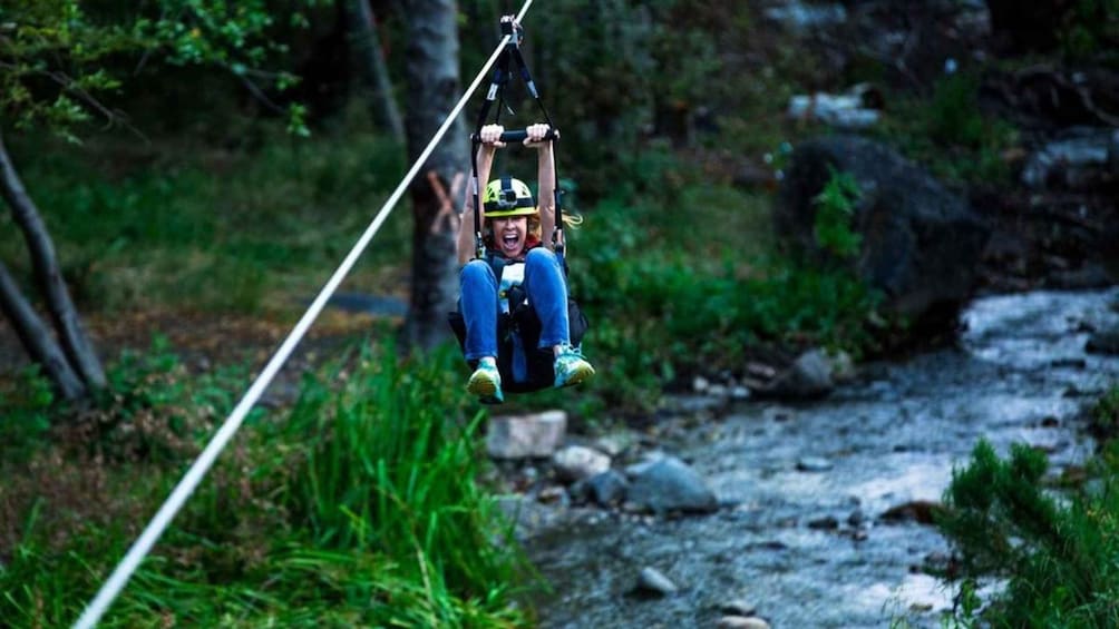 A person on a zip line over a rocky stream in a forest. 2