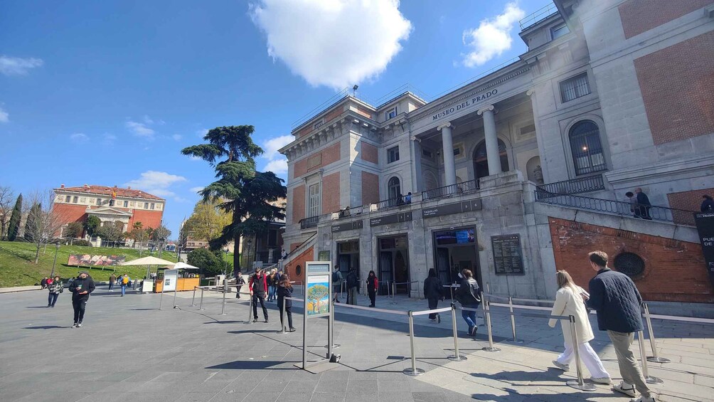 A plaza with a museum entrance, people walking, and a large tree. 3