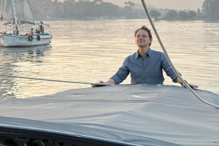 Une personne à bord d’un bateau à voile, sur une rivière paisible, avec une côte lointaine à l’horizon. 2
