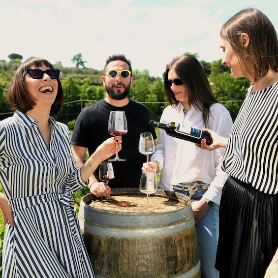 Four people standing around a wooden barrel, holding wine glasses and a bottle. 5