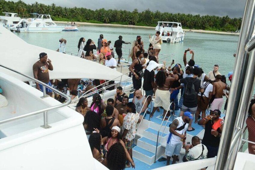 A crowded boat with people standing and sitting, surrounded by calm water and distant greenery. 2