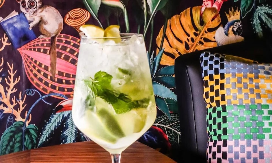 A cocktail with lime and mint, a colorful chair, and a vibrant mural in the background. 4
