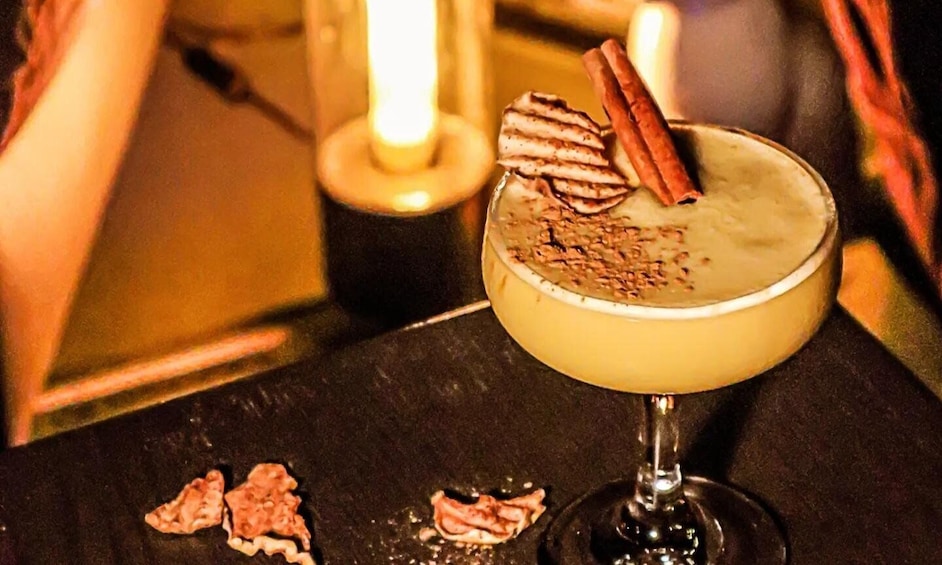 A cocktail with a cinnamon stick garnish on a dark surface. 2