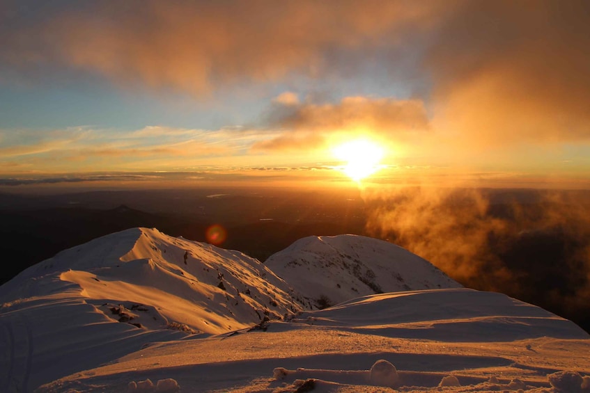 A snow-covered mountain peak at sunrise with the sun visible through the clouds. 4