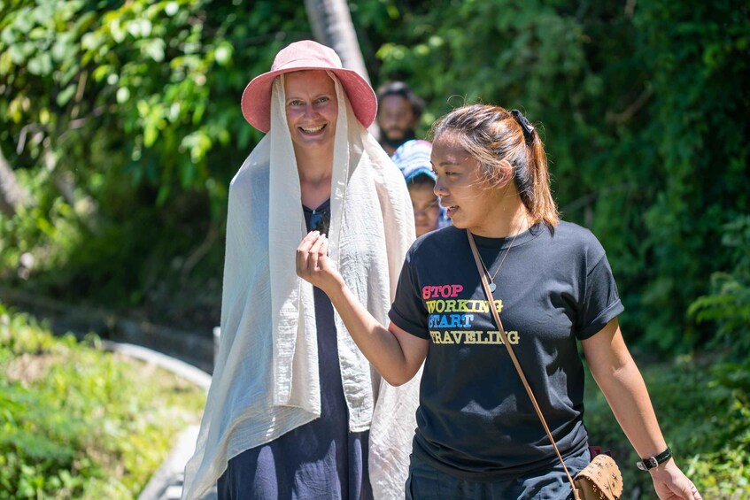 Two people walking outdoors, one wearing a hat and a shawl, and the other in a t-shirt with a travel-related slogan. 3