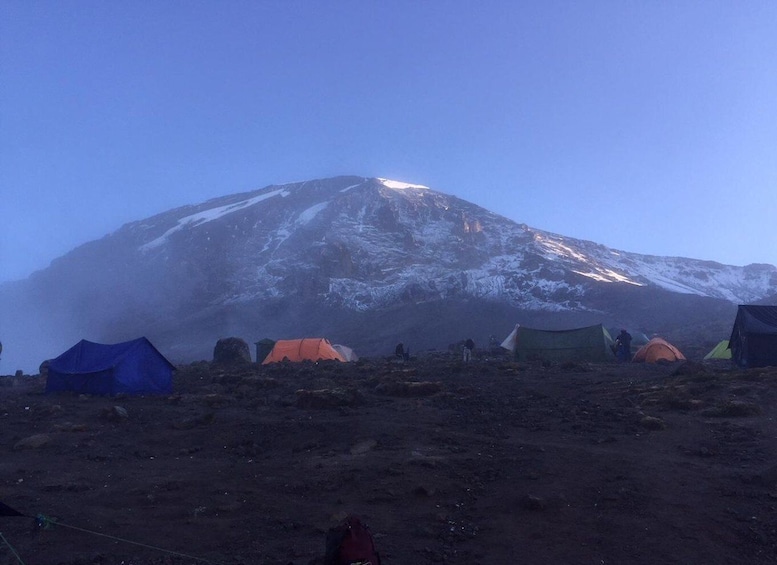 A mountain with snow at its peak and several tents on the ground. 1