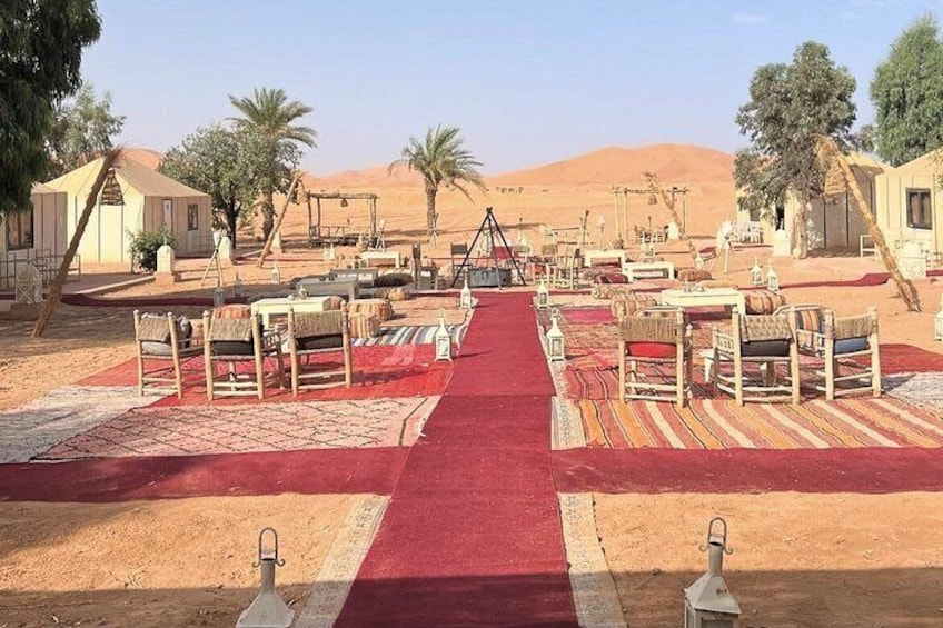 A desert campsite with tents, tables, chairs, and a red carpet walkway. 5