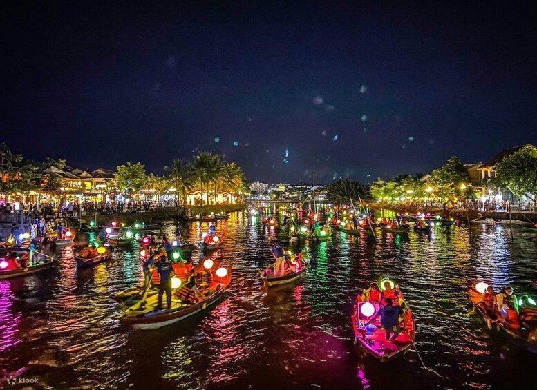 A nighttime river scene with illuminated boats and a crowd of people along the riverbank. 3