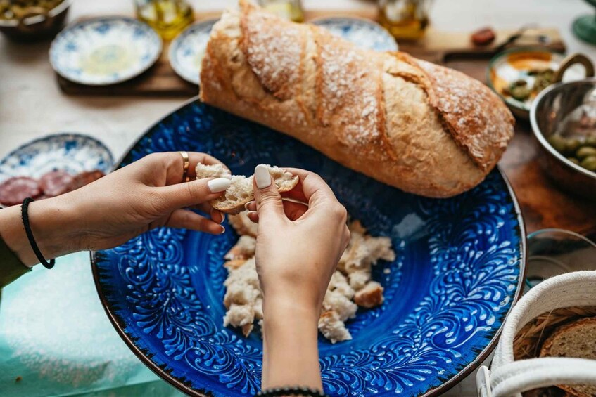 Hands breaking bread on a blue plate with a loaf of bread. 4