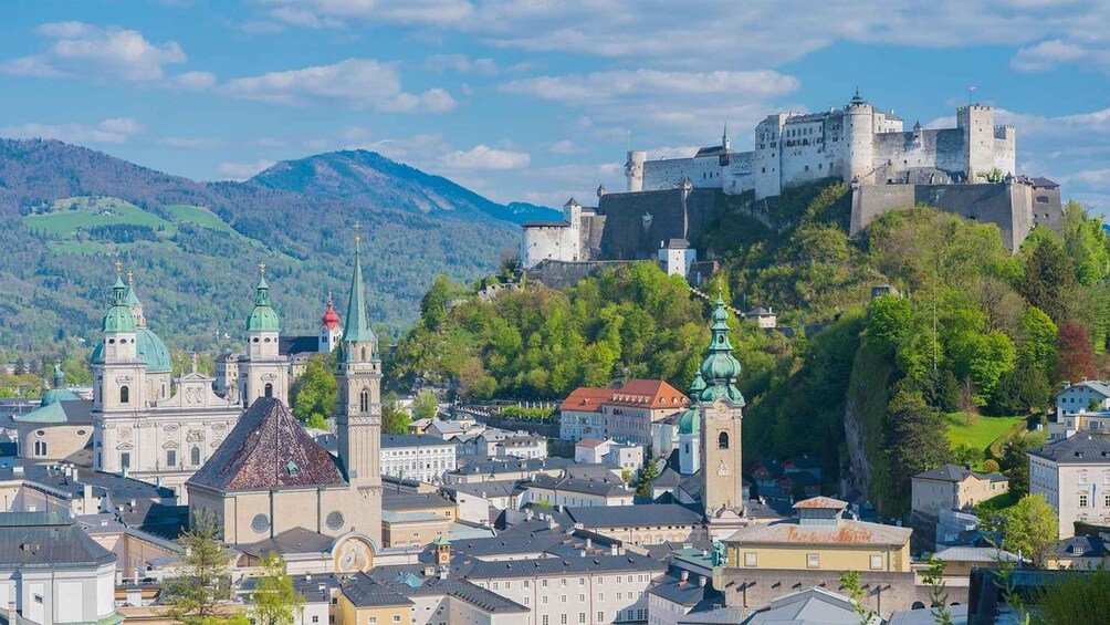 A historic town with a prominent castle on a hill, surrounded by lush greenery and a church with distinctive green domes. 3