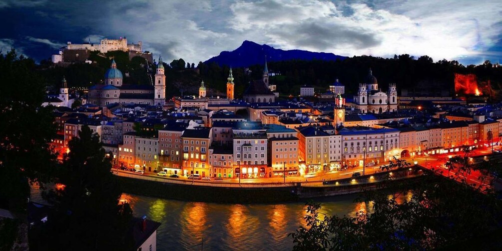 A cityscape with a prominent castle on a hill, a river reflecting lights, and a mountain in the background. 5