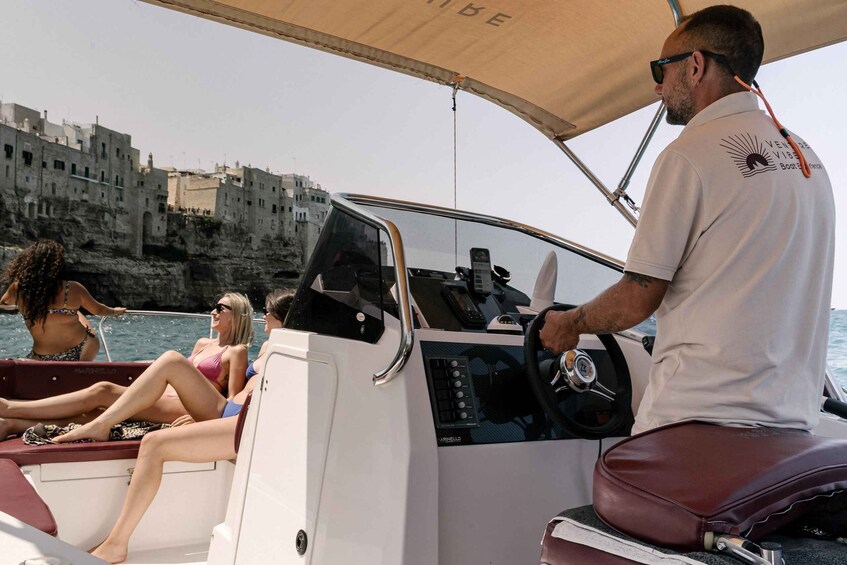 A boat with a driver steering, passengers on deck, and a coastal town in the background. 5