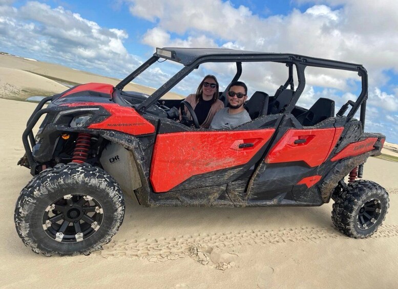 A red and black off-road vehicle parked on a sandy beach with dunes in the background. 1