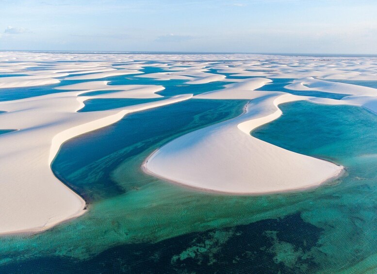 A vast aerial view of white sand dunes with clear blue waters between them. 2