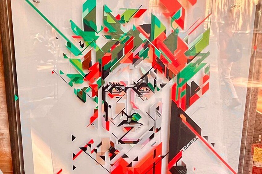 Obra de arte abstracta geométrica con una figura central que recuerda a un rostro, rodeada de formas angulares en rojo, verde y negro. 5