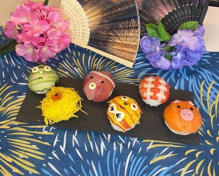 Sushi with animal faces on a black slate, surrounded by flowers and a fan. 3