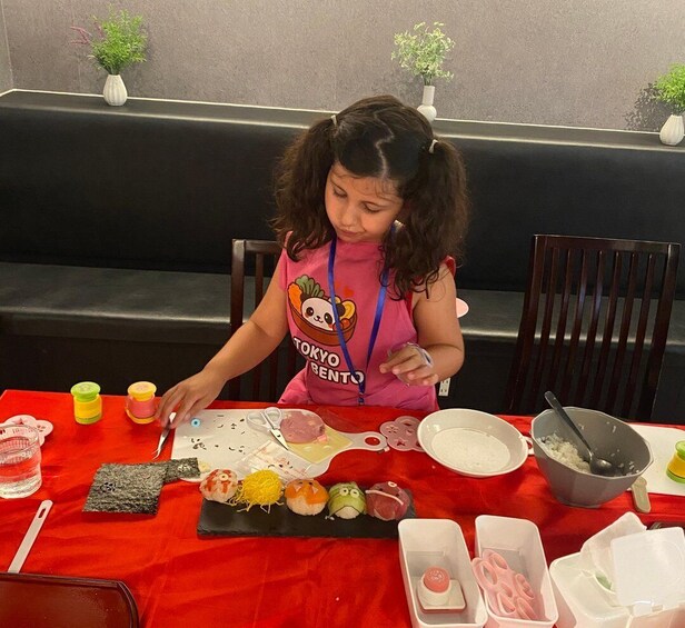 A child at a table with sushi, a red tablecloth, and a bowl of rice. 5