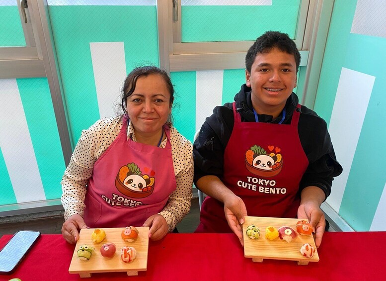 Two people holding wooden boards with sushi pieces, wearing aprons with animal designs. 2