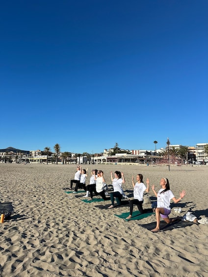 A group of people performing yoga on a beach with buildings in the background. 1