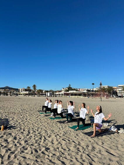 A group of people practicing yoga on a sandy beach with buildings in the background. 3