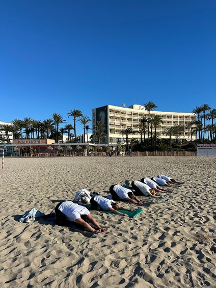 A group of people performing yoga on a sandy beach with a hotel and palm trees in the background. 4