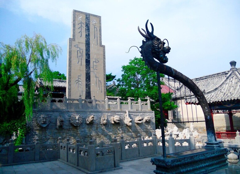 A traditional Chinese architectural structure with a dragon statue and a tall pillar with inscriptions. 2