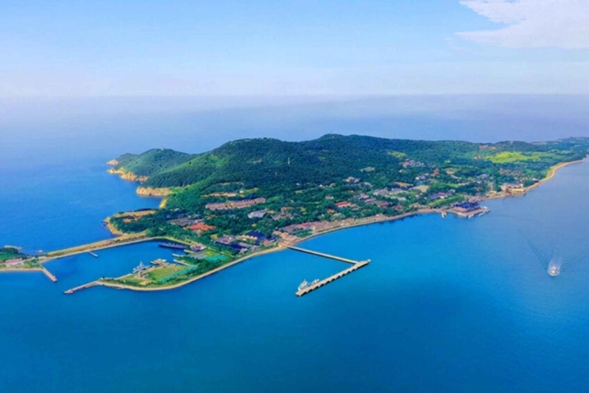 An aerial view of a coastal island with a pier, dense greenery, and a clear blue sea. 4