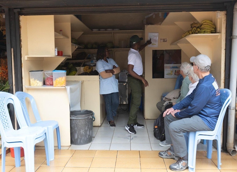 A small outdoor food stall with a person serving customers, a trash can, and a few seated customers. 3