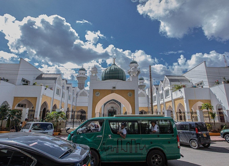 A mosque with a green dome and minarets, surrounded by white buildings and parked cars. 4