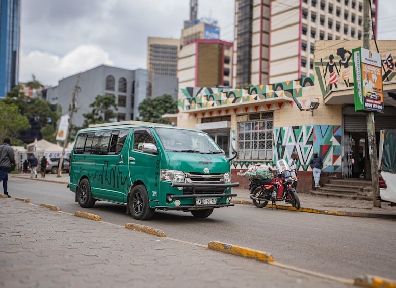 A green minibus on a city street with buildings and a motorcycle in the background. 5