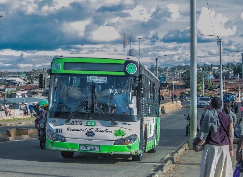 A green and white bus with 'Committed To Travellers' on the front, driving on a city street. 1