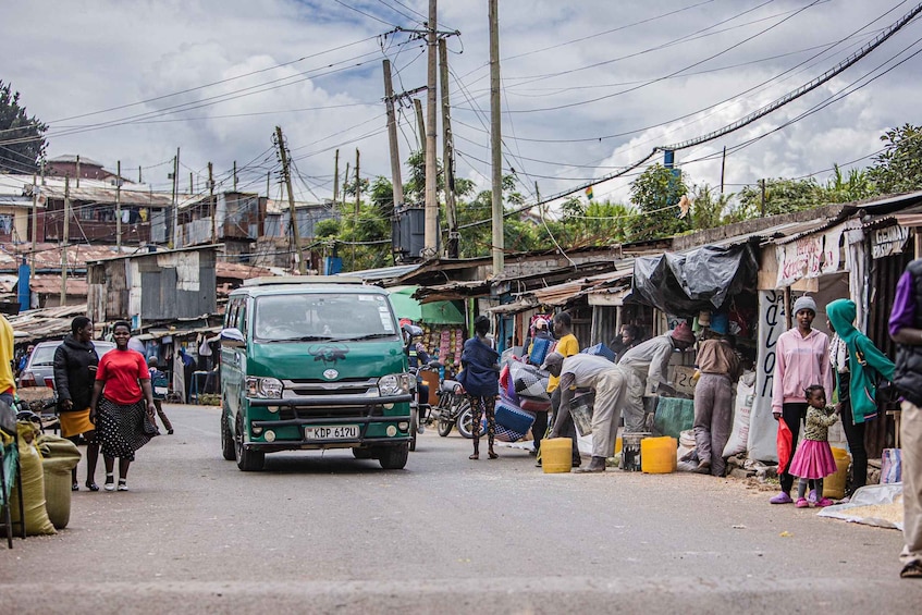 A bustling street scene with a green car, people, and makeshift stalls. 2