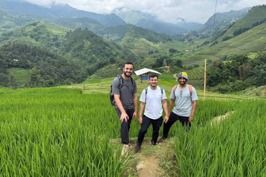 Tres personas de pie en un exuberante campo de arroz con montañas al fondo. 4